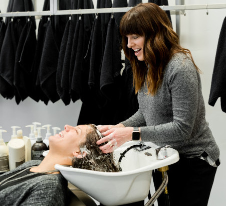 Une coiffeuse lave les cheveux d'une femme. Elles discutent avec un grand sourire.